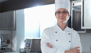 A chef standing with arms crossed in a kitchen.